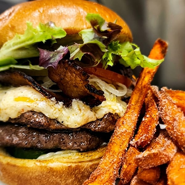 Double cheeseburger with bacon, lettuce, onion, and a side of sweet potato fries.