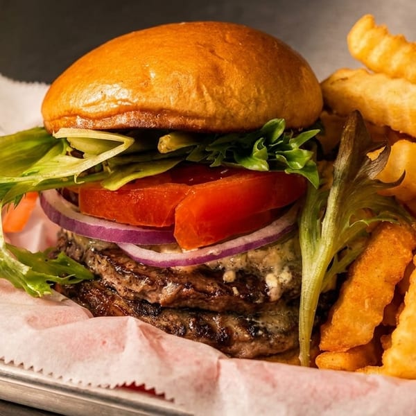 Double cheeseburger with lettuce, tomato, onion, and crinkle-cut fries in a metal basket.