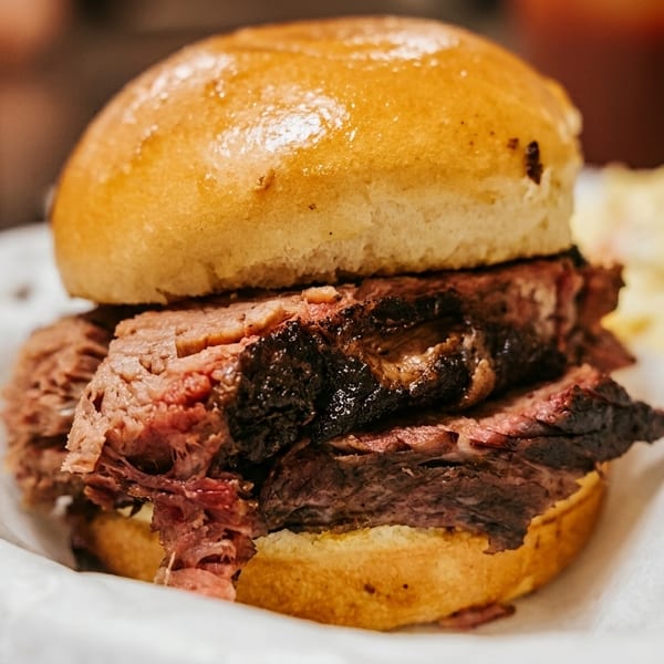 Close-up of a brisket sandwich on a bun, served in a paper-lined basket with sides.