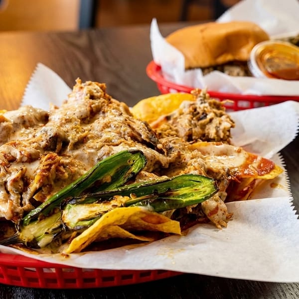 Loaded nachos with grilled jalapeños and a burger with greens in the background.