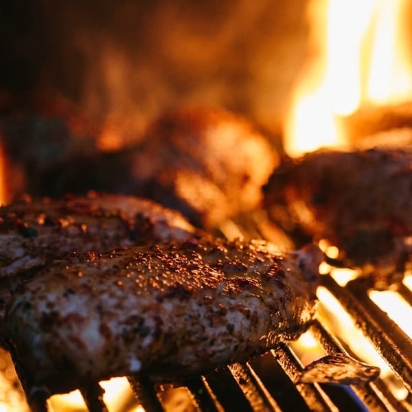 Seasoned chicken breasts grilling over open flames on a barbecue.