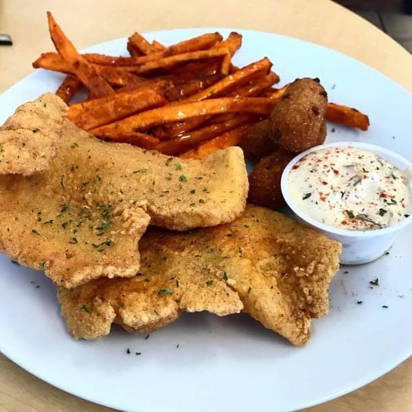 Fried fish fillets with sweet potato fries, hush puppies, and tartar sauce on a white plate.