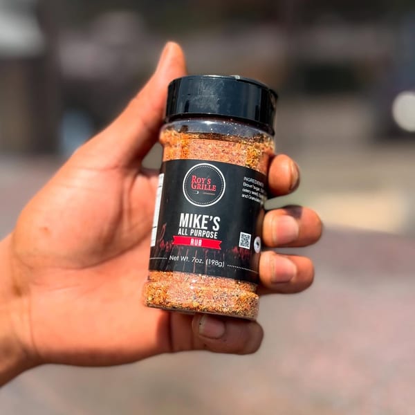 A hand holds a bottle of Roy's Grille "Mike's All Purpose Rub" seasoning blend.