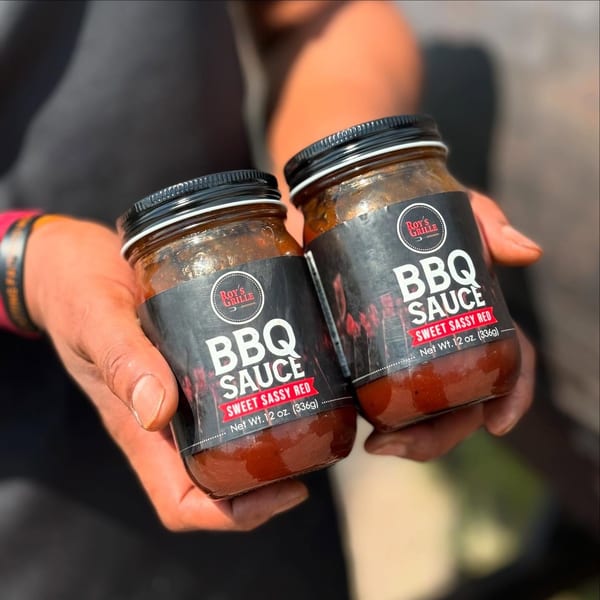 Two hands holding two jars of Roy's Grille Sweet Sassy Red BBQ Sauce.